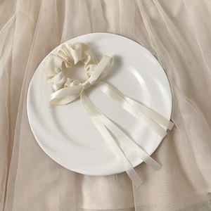Detail of cream satin bow scrunchie with long ribbons on a decorative ceramic plate
