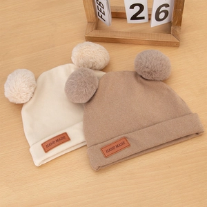 Detailed close-up of knit baby hats with double pom-poms and handmade leather tags