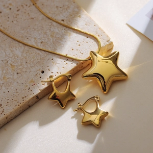 Polished gold star earring and necklace set displayed on beige marble background