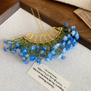 Detail of elegant gold wavy hair pin with delicate blue and white flower decorations