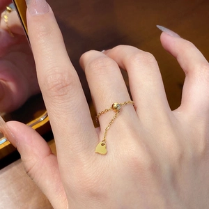 Close-up of golden chain ring featuring heart pendant and green zircon detail