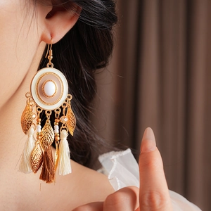 Close-up of bohemian enamel tassel earrings with gold leaf charms worn by a model