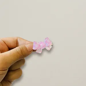 Detailed view of a small pink bow-shaped hair clip held by hand on a white desk