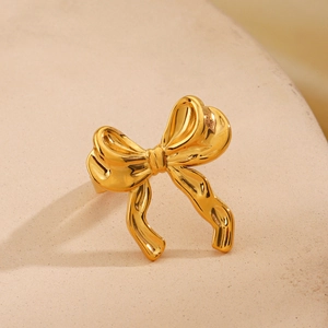 Polished 18K gold plated stainless steel bow ring on minimalist textured background