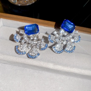 Detailed view of silver fan-shaped earrings with blue gems and diamonds in a jewelry box