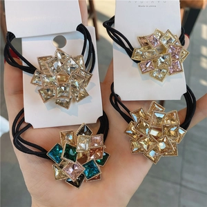 Detailed view of four colorful rhinestone flower elastic hair ties in hand