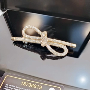 Detail view of a luxury gold bow hair clip with sparkling rhinestones on black background