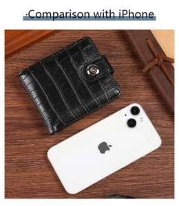 Size comparison of crocodile pattern black wallet next to an iPhone on a wooden desk