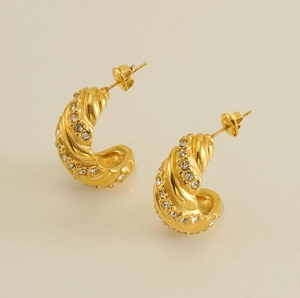 Gros plan détaillé de boucles d'oreilles dorées forme C avec texture spirale et zircones