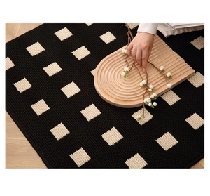 Detail of black woven entryway rug with cream square pattern on light wood floor