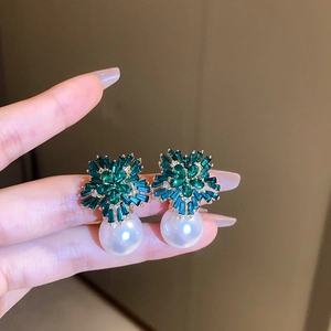Macro shot of green crystal flower earrings with a large white pearl drop in hand