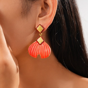 Close-up of red fan-shaped enamel earring with golden metal texture on model's ear