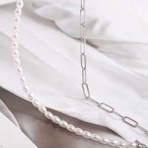Detailed macro view of layered necklace featuring white oval pearls and silver paperclip chain