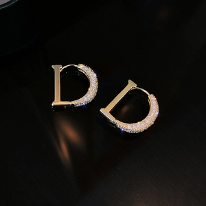 Elegant gold letter D earrings with white zircon stones on a reflective black background