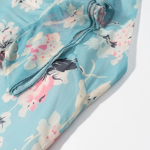 Dettaglio del tessuto floreale in chiffon azzurro con bordi a balze e cuciture fini