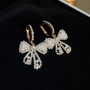 Close-up of golden bow earrings with sparkling rhinestones and pearls on black velvet