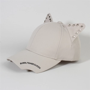 Detail of light beige baseball cap featuring cat ears with metal studs and printed text