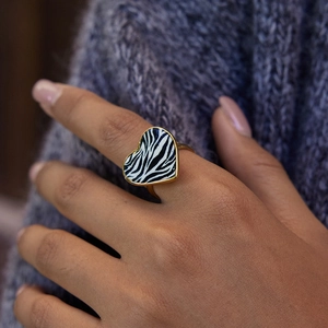 Golden heart-shaped ring with zebra pattern worn on hand over a knit sweater