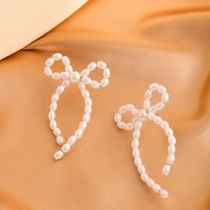Macro detail of elegant bow-shaped pearl earrings on a luxurious gold satin background