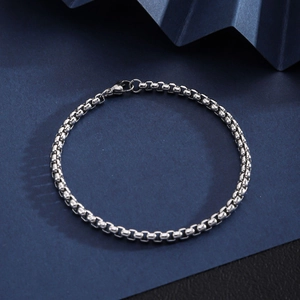 Macro detail of silver stainless steel box chain bracelet featuring a lobster clasp closure