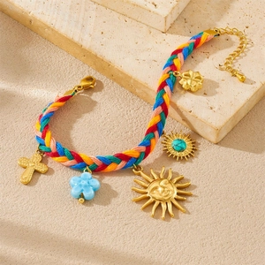 Colorful woven rope bracelet with gold cross and sun charms on a stone surface