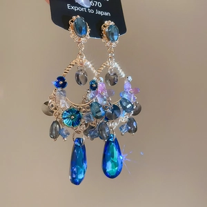 Macro shot of blue crystal drop earrings with purple flower details and gold chain