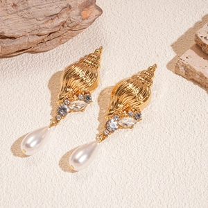 Golden shell earrings with white drop pearls and crystal accents on a sandy background