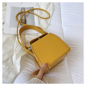 Macro detail of a bright yellow PU leather box bag with silver metal feet on white fabric