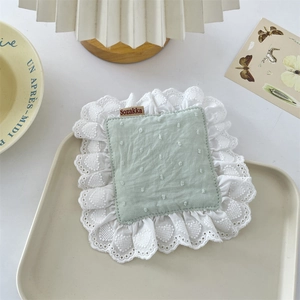 Close-up of light green fabric coaster with white ruffled lace and heart patterns