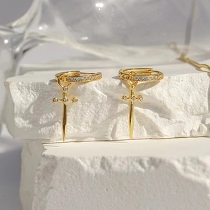 Detail of gold dagger earrings with white zircons on a white minimalist stone base