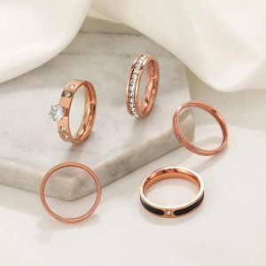 Detailed set of five rose gold rings featuring black enamel and crystals on marble