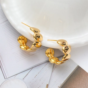 Polished 18K gold-plated copper C-shaped earrings with segmented geometric design on a plate