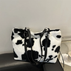 Chic black and white cow print plush tote bag for women on a sleek leather chair