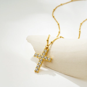 Macro detail of a golden cross pendant featuring clear crystals and a stylish satelite chain