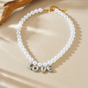 White pearl necklace with silver LOVE letter pendant on a textured beige background