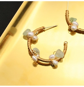 Macro shot of handmade gold wire-wrapped C-shape earrings with pearls and green stones