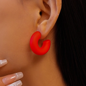 Close-up of a matte red C-shaped acrylic hoop earring worn on model with high texture