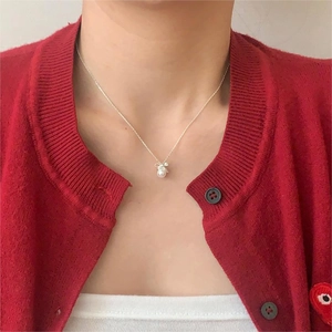 Detailed view of a silver bow necklace with a white pearl pendant on a female model