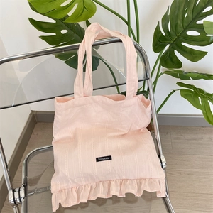 Pink canvas tote bag with ruffled hem and Sozakka label on a stylish transparent chair