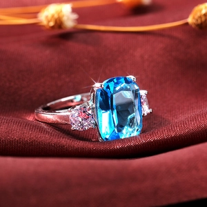 Macro d'une bague avec zircon bleu rectangulaire et pierres roses sur satin rouge