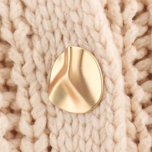Artistic gold matte irregular wave earrings styled on a beige chunky knit sweater background