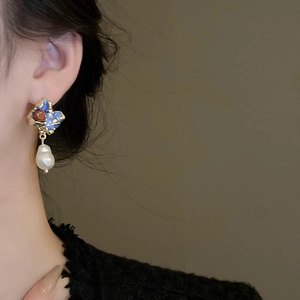 Close-up of a French retro earring with blue enamel, gold alloy and baroque pearl detail