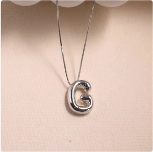 Detailed close-up of a silver balloon style letter G pendant with realistic texture