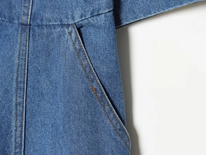 Detail der Jeanskleid-Tasche mit orangefarbenen Kontrastnähten auf blauem Denim-Stoff