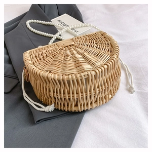 Detail of handmade semi-circular woven bamboo bag with pearl strap on a grey blazer
