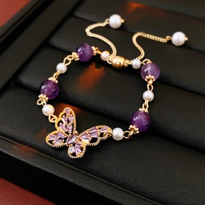 Detail of gold butterfly bracelet with purple crystals and white pearls on black tray