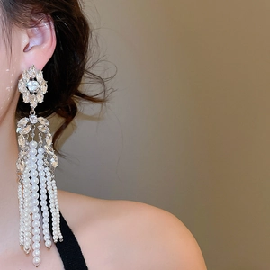 Detail of floral crystal studs with long pearl tassels worn by a model in warm light