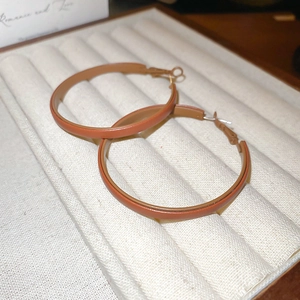 Macro detail of brown leather wrapped hoop earrings with gold-toned metal accents