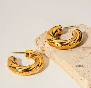 Polished 18K gold-plated twisted C-shaped hoop earrings on a textured stone display