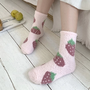 Detail of pink coral fleece socks featuring strawberry embroidery on light wood floor